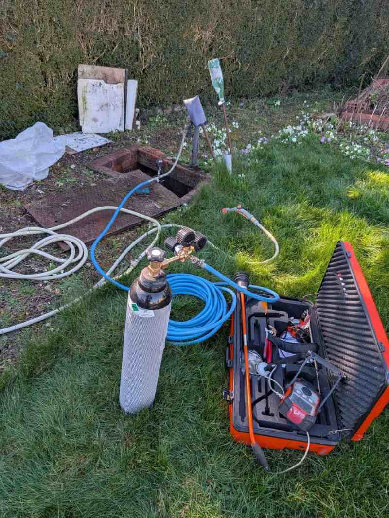 Recherche de fuite enterrée par gaz traceur dans un jardin, regard en brique ouvert