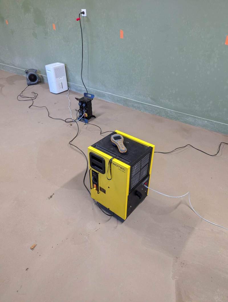 Déshumidificateur et ventilateur d’assèchement en marche dans une salle vide, un humidimètre posé dessus