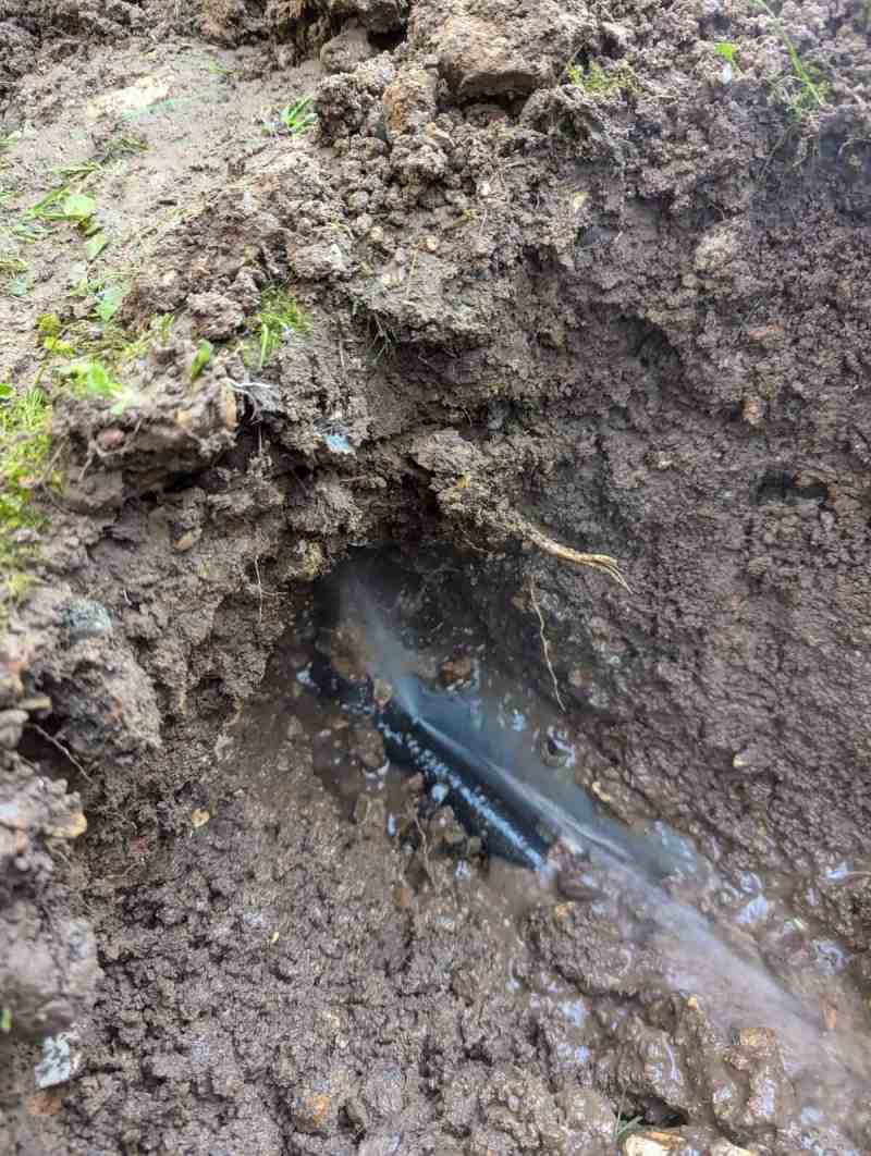 Canalisation enterrée percée dans une fouille, avec un jet d’eau