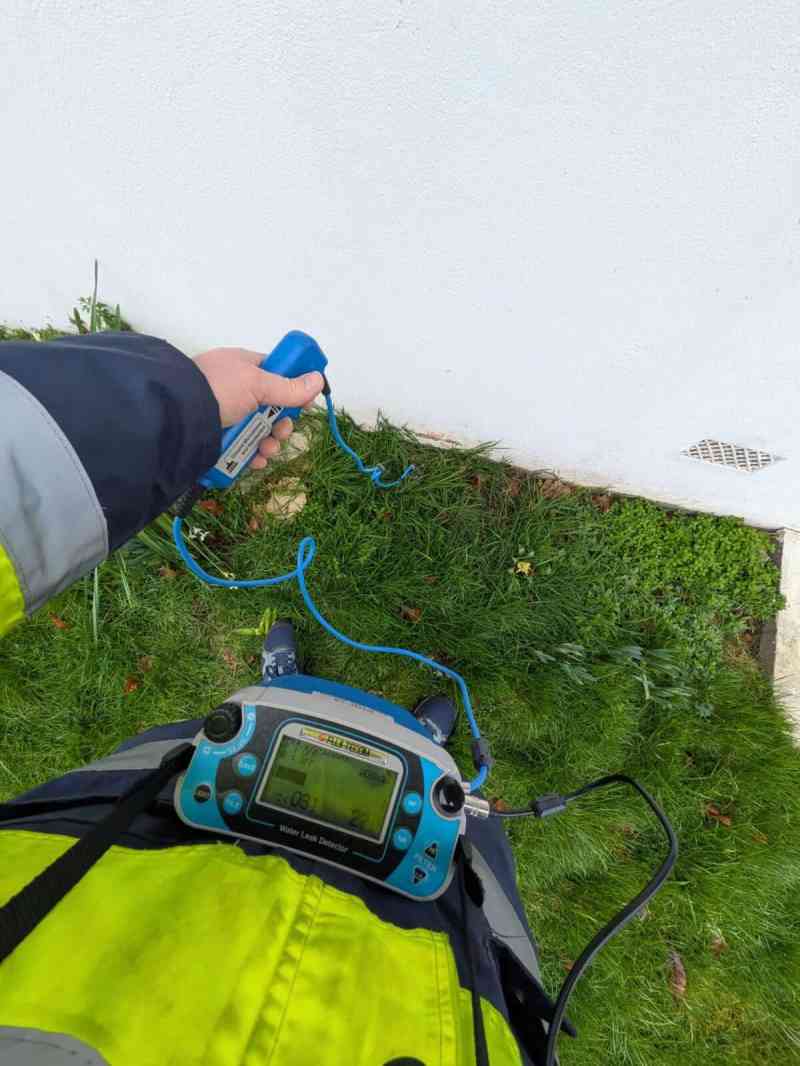 Technicien avec un micro de sol et un détecteur acoustique sur une pelouse, le long d’un mur blanc
